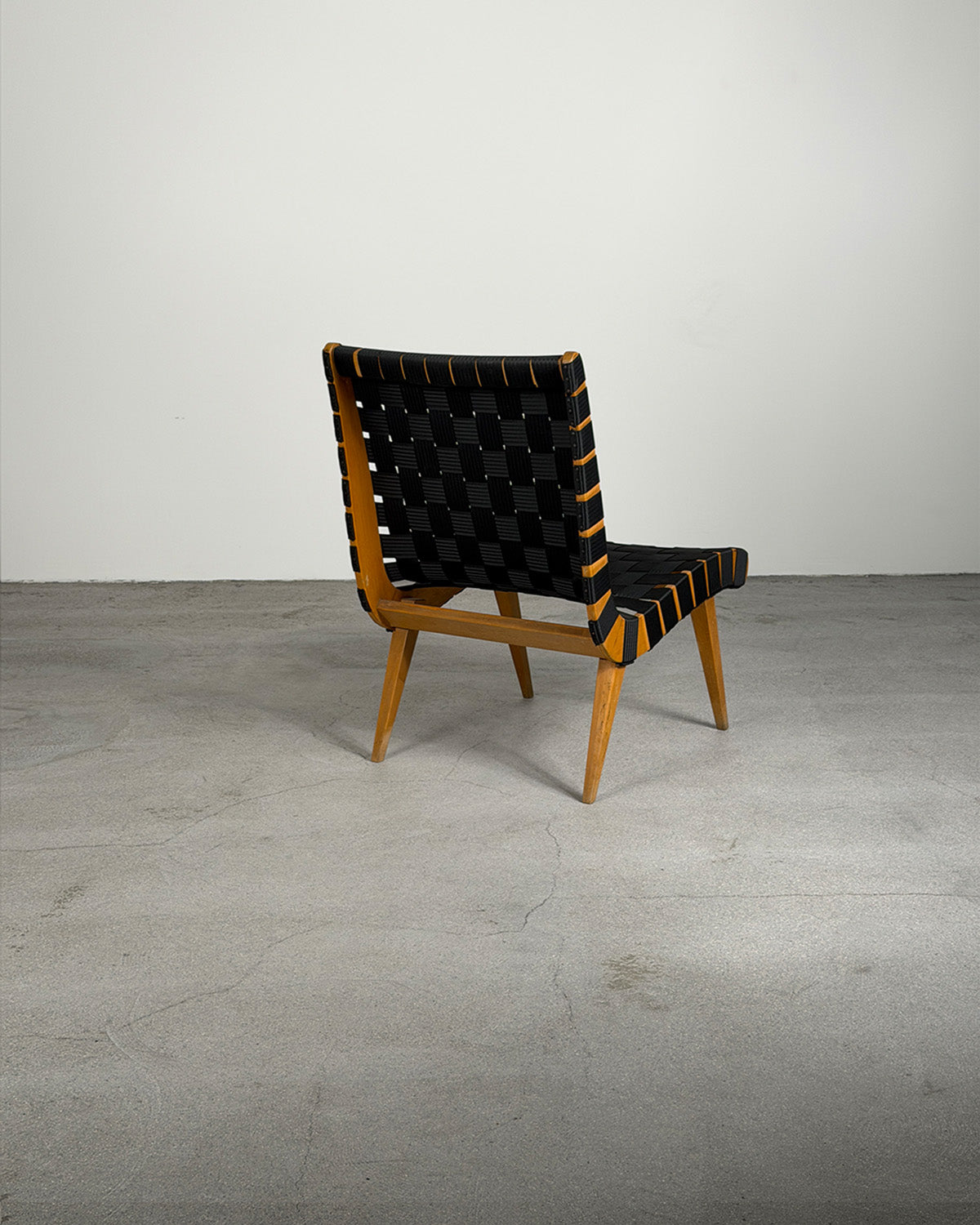 Chair with black woven backrest and wooden frame on a gray floor.