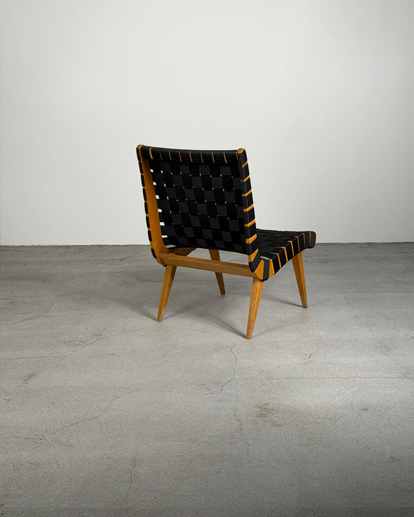 Chair with black woven backrest and wooden frame on a gray floor.