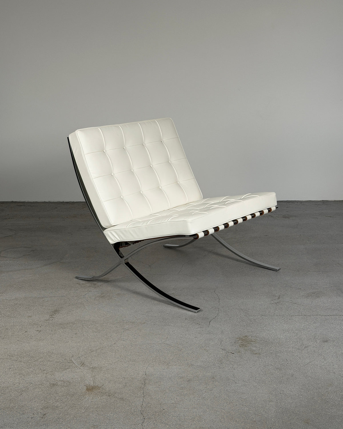 A modern White Leather Barcelona Chair by Ludwig Mies van der Rohe for Knoll with white tufted leather upholstery and a curved chrome steel base, photographed in a minimalist gray studio setting.